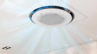 Samsung 360-Grad-Kassette an der Decke, mit visualisierter Luftzirkulation in alle Richtungen für gleichmäßige Raumklimaverteilung. Moderne Badezimmerbeleuchtung umgibt das Gerät